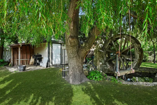 a backyard of a house with table and chairs a barbeque and a large tree