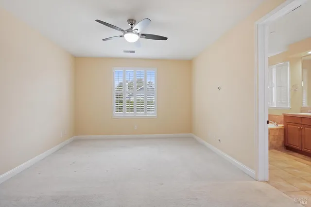 an empty room with chandelier fan and windows