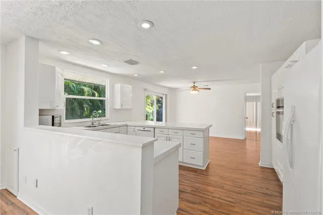 a kitchen with stainless steel appliances granite countertop a refrigerator a sink dishwasher and white cabinets with wooden floor