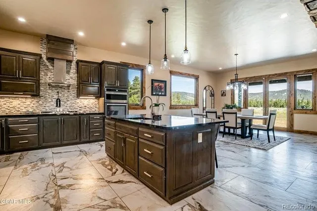 a kitchen with stainless steel appliances granite countertop wooden cabinets a sink a stove a dining table and chairs