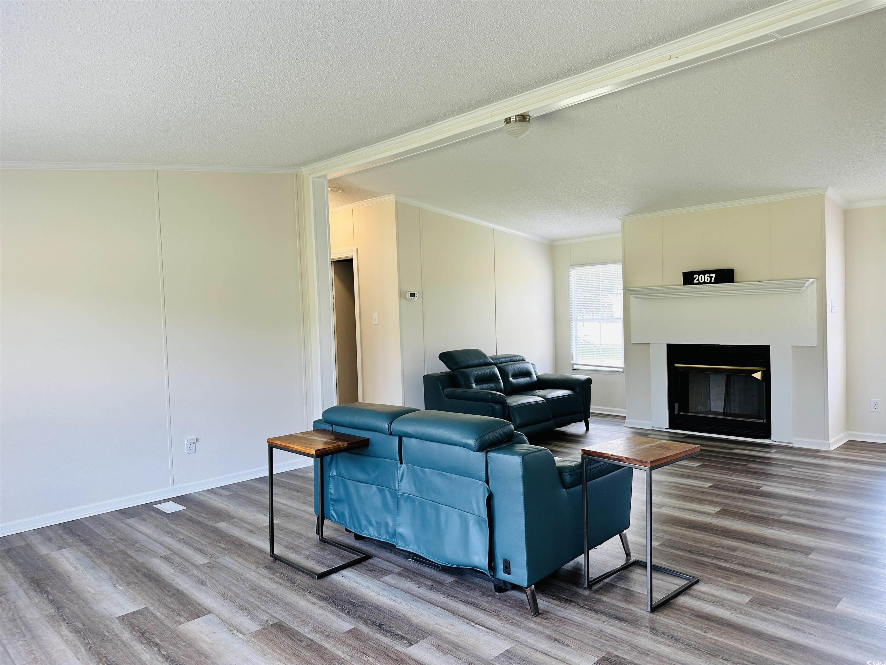 2067 Willow Creek Road Effingham, SC 29541 - Photo 21 of 40 Living area with crown molding, wood finished floors, a glass covered fireplace, a textured ceiling, and a decorative wall