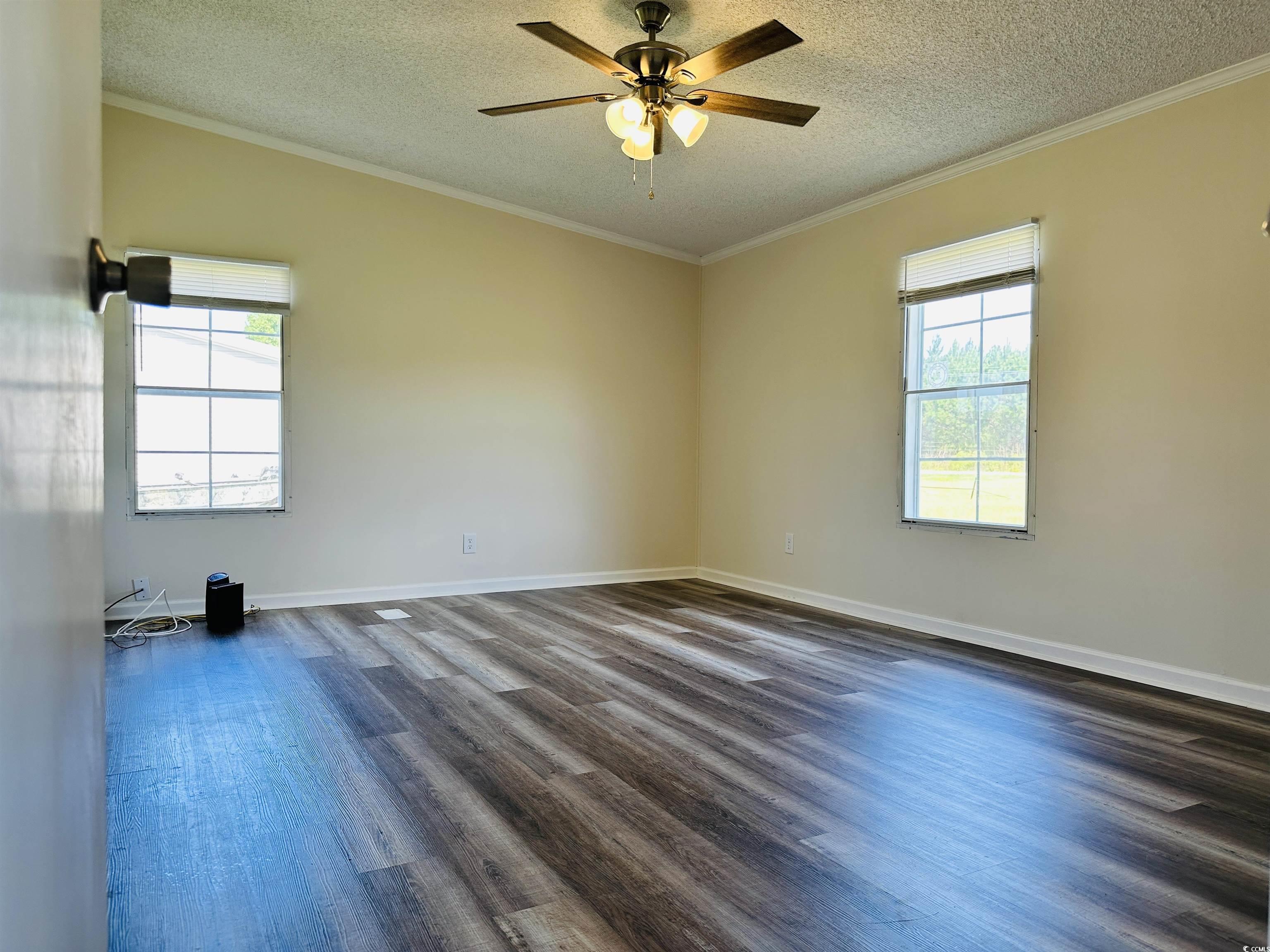 2067 Willow Creek Road Effingham, SC 29541 - Photo 37 of 40 Empty room featuring crown molding, dark wood-type flooring, healthy amount of natural light, a textured ceiling, and a ceiling fan