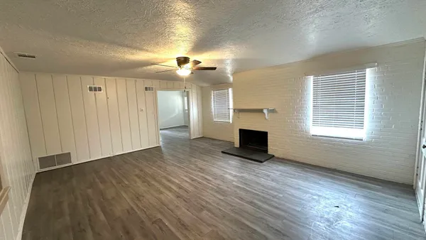 an empty room with wooden floor fireplace and windows