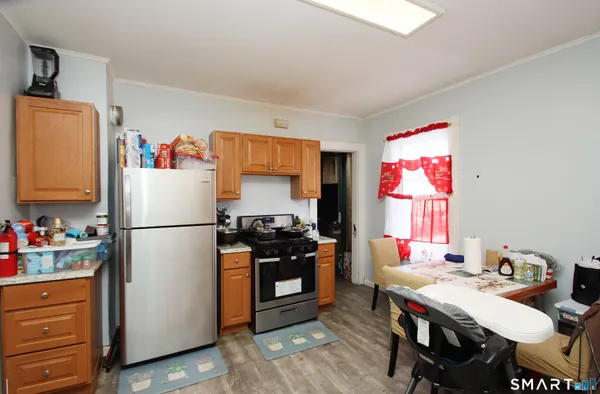 a white kitchen with a refrigerator a stove a sink and a dining table with wooden floor