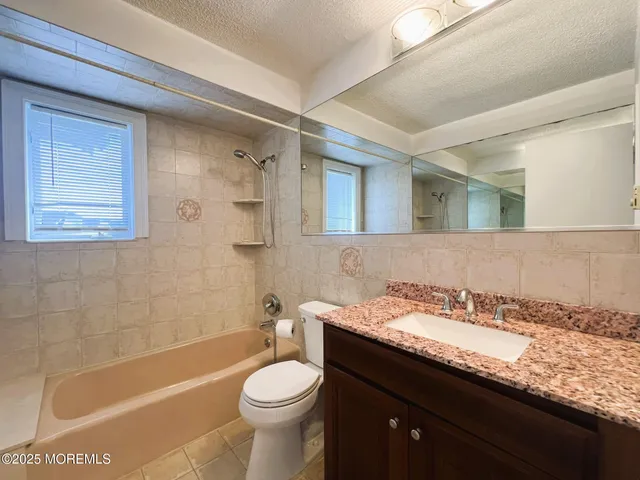 a bathroom with a granite countertop sink a toilet a mirror and bathtub