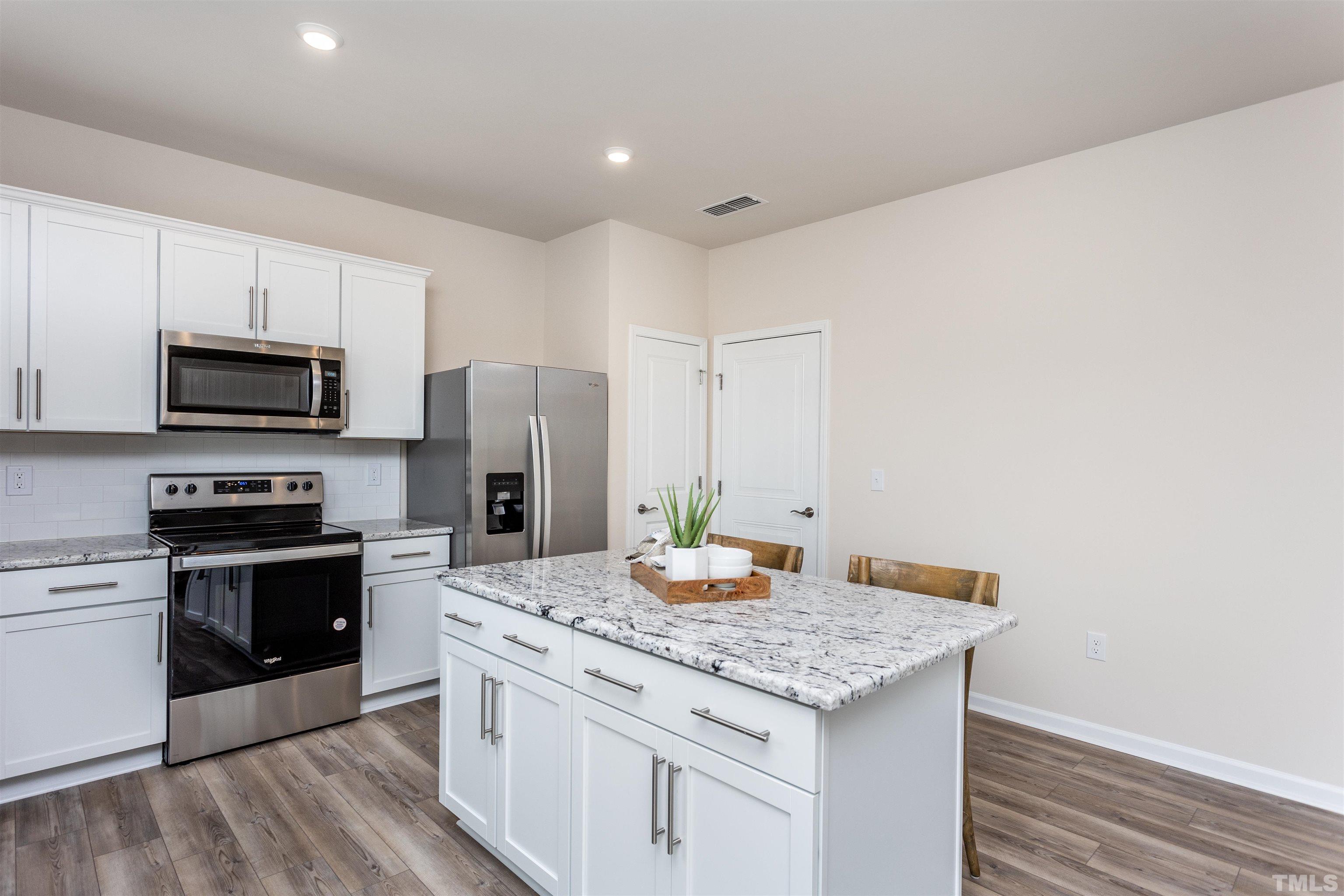 3469 Dragonfly River Raleigh, NC 27604 - Photo 16 of 26 a kitchen with stainless steel appliances kitchen island granite countertop a stove top oven a sink dishwasher a refrigerator and a dining table with wooden floor