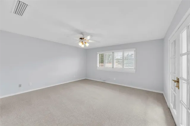 an empty room with chandelier fan and windows