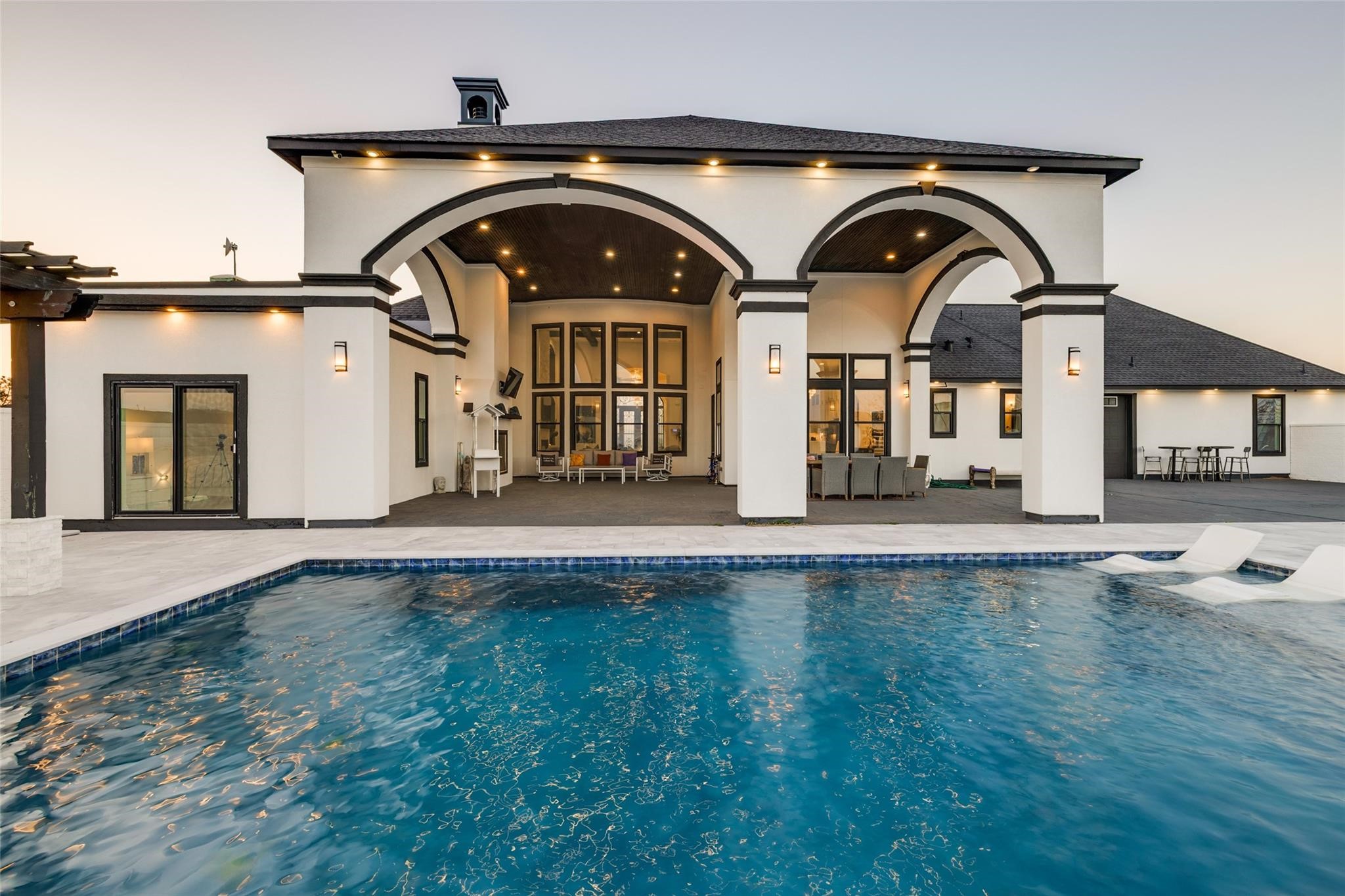 4821 Walters Road Richmond, TX 77469 - Photo 7 of 50 This stunning heated luxury pool creates a true resort-style experience with sleek modern design, expansive lounging areas, and breathtaking sunset views. Featuring elegant marble-style decking, in-water chaise loungers, ambient accent lighting, and a striking stone water feature, the space was thoughtfully designed for both relaxation and entertaining. A covered pergola lounge adds the perfect setting for evening gatherings, while the oversized pool offers a seamless blend of comfort & privacy.