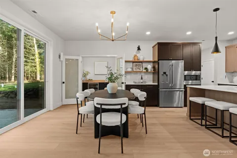 a kitchen with stainless steel appliances kitchen island granite countertop a refrigerator a stove a microwave oven a dining table and chairs with wooden floor
