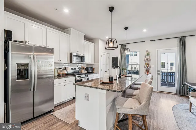 a kitchen with stainless steel appliances kitchen island granite countertop a refrigerator a stove a sink a dining table and chairs with wooden floor