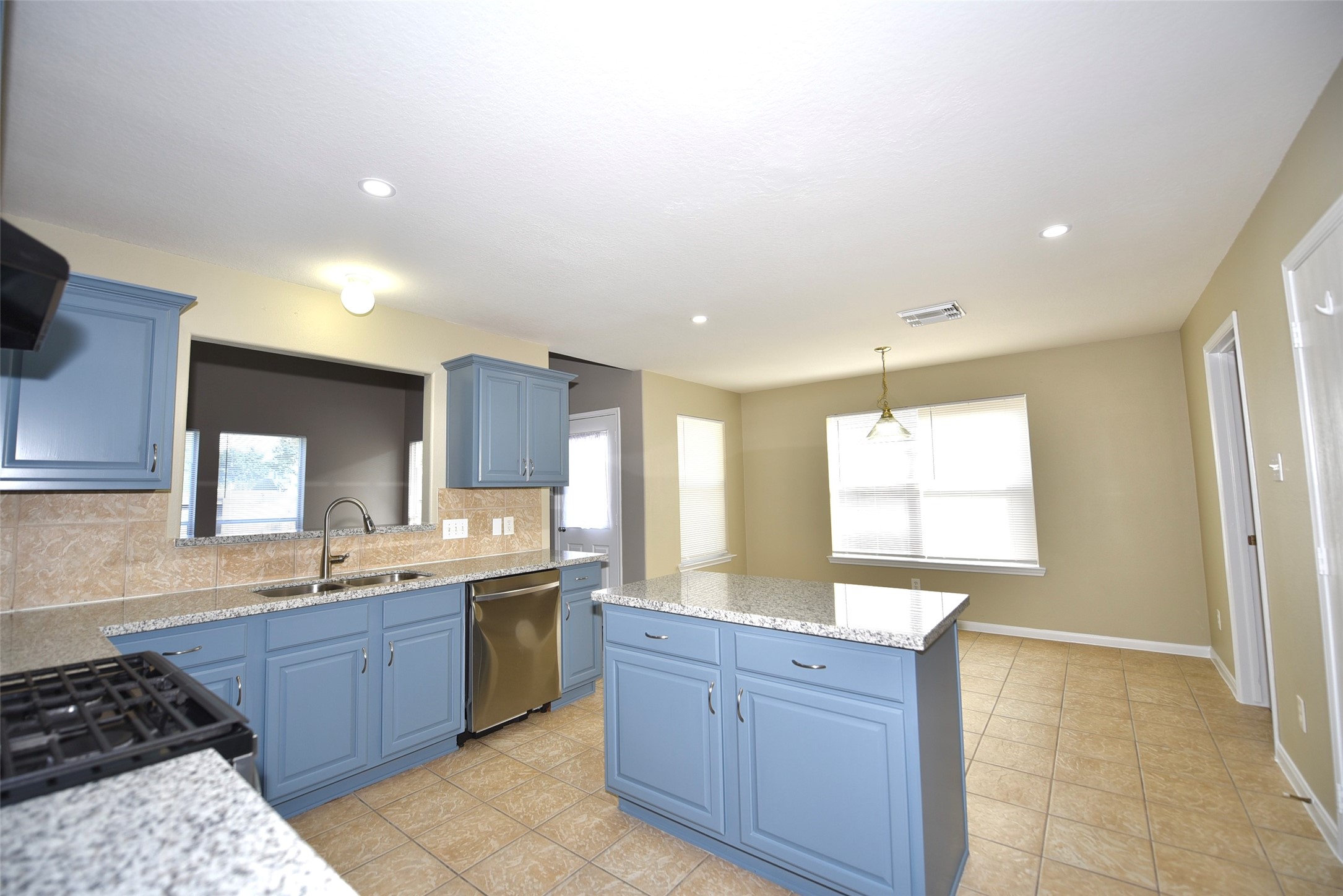 9611 Babbling Spring Court Tomball, TX 77375 - Photo 10 of 31 Bright kitchen with blue cabinets, granite countertops, and tile flooring. Includes a central island, stainless steel appliances, and a cozy dining area with natural light.
