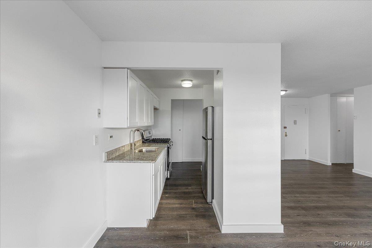 2550 Olinville Avenue, Unit 8H Bronx, NY 10467 - Photo 13 of 24 Kitchen featuring white cabinetry, light stone countertops, appliances with stainless steel finishes, and dark wood finished floors