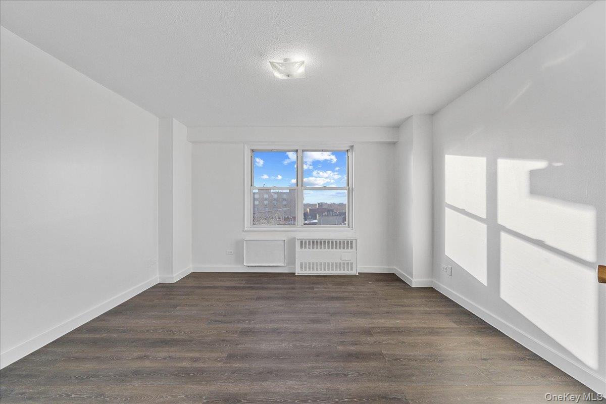 2550 Olinville Avenue, Unit 8H Bronx, NY 10467 - Photo 15 of 24 Empty room featuring radiator heating unit, dark wood-type flooring, and a textured ceiling