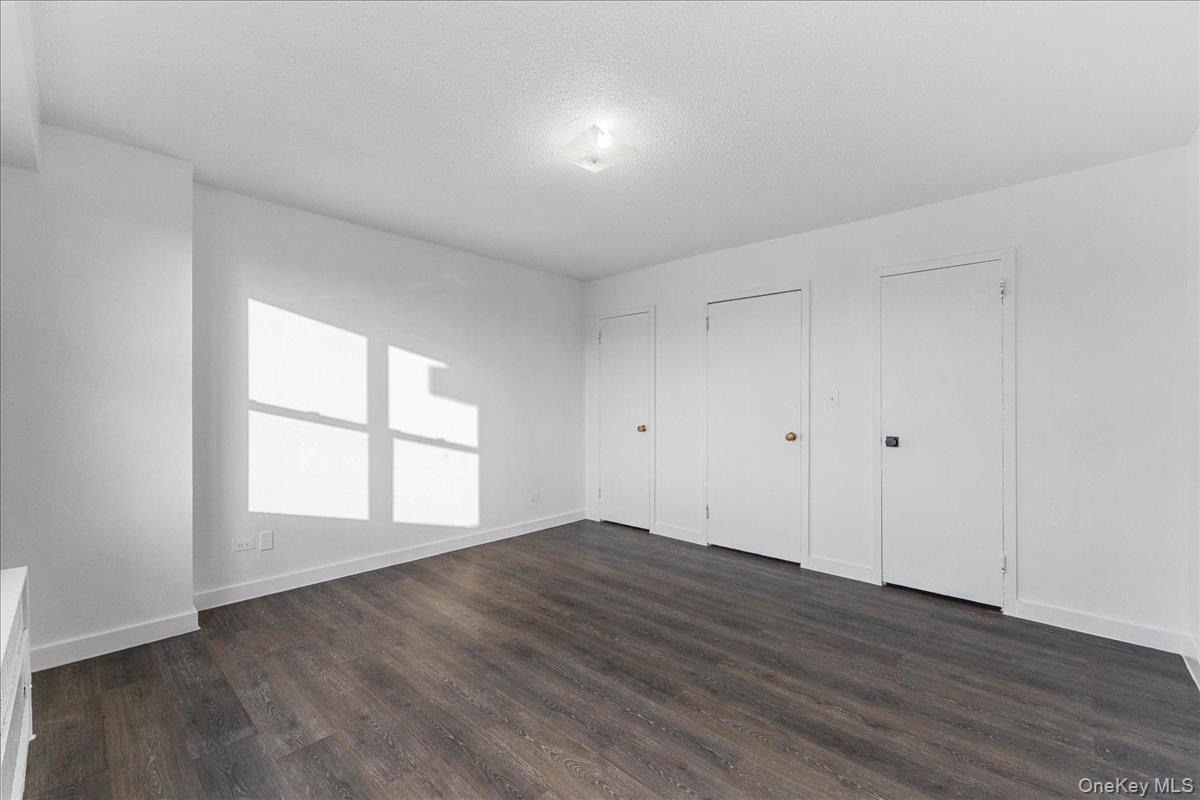 2550 Olinville Avenue, Unit 8H Bronx, NY 10467 - Photo 17 of 24 Unfurnished bedroom featuring dark wood-type flooring, a textured ceiling, and multiple closets