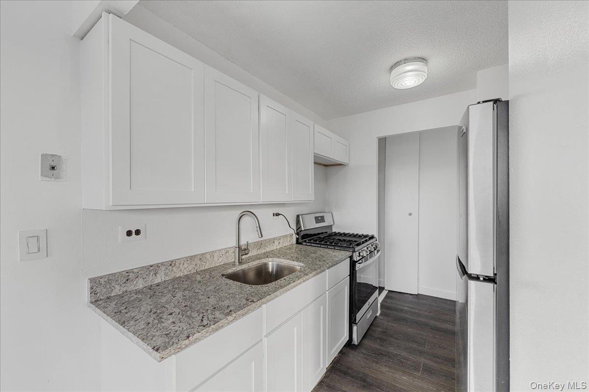 2550 Olinville Avenue, Unit 8H Bronx, NY 10467 - Photo 5 of 24 Kitchen featuring stainless steel appliances, white cabinets, light stone countertops, dark wood finished floors, and a textured ceiling