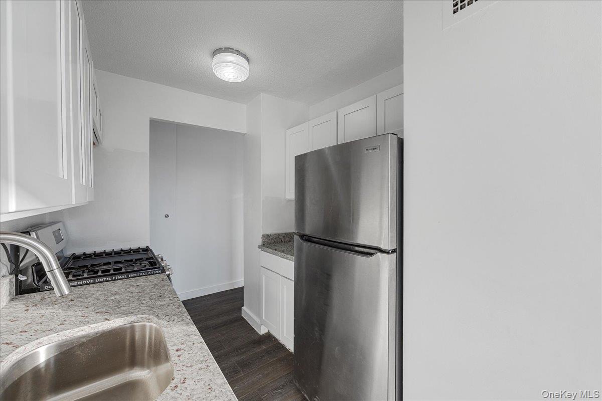 2550 Olinville Avenue, Unit 8H Bronx, NY 10467 - Photo 6 of 24 Kitchen with freestanding refrigerator, a textured ceiling, light stone countertops, white cabinetry, and range with gas stovetop