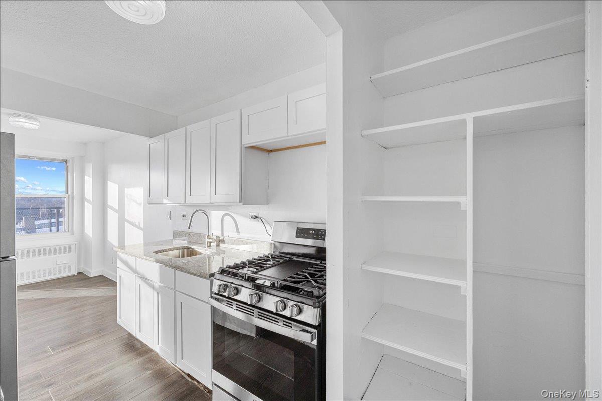 2550 Olinville Avenue, Unit 8H Bronx, NY 10467 - Photo 7 of 24 Kitchen featuring appliances with stainless steel finishes, white cabinetry, light stone countertops, radiator, and light wood-type flooring