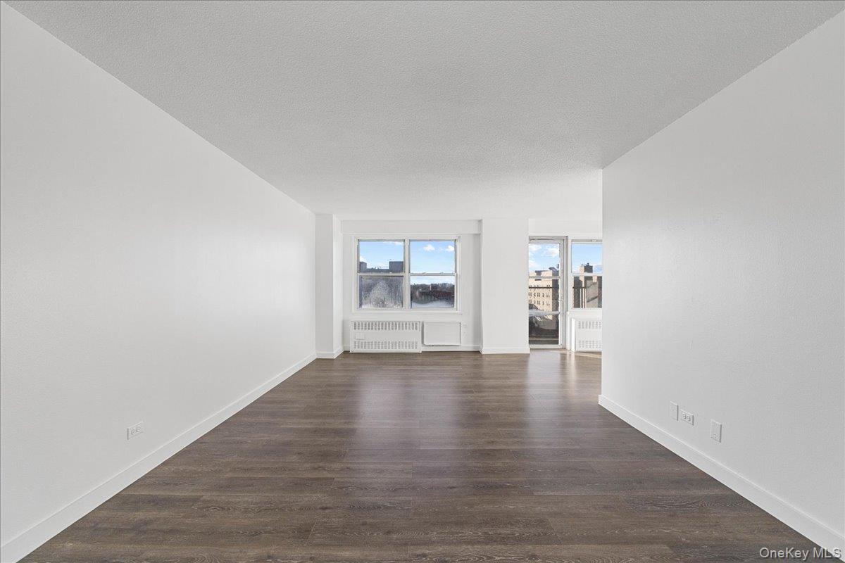 2550 Olinville Avenue, Unit 8H Bronx, NY 10467 - Photo 8 of 24 Unfurnished room with dark wood-type flooring, radiator heating unit, and a textured ceiling