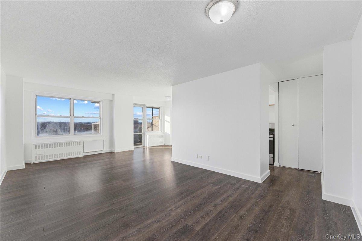 2550 Olinville Avenue, Unit 8H Bronx, NY 10467 - Photo 9 of 24 Spare room featuring radiator heating unit, dark wood-style floors, and a textured ceiling