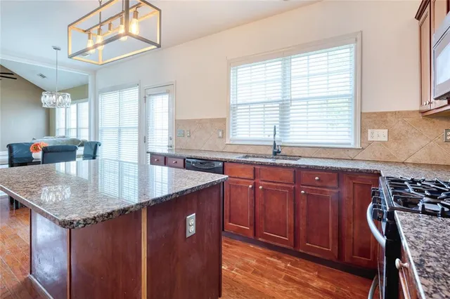 a kitchen with stainless steel appliances granite countertop a sink a window and wooden cabinets