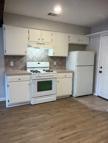 a white kitchen with wooden floor and white stainless steel appliances