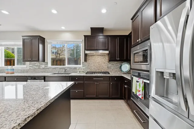 a large kitchen with stainless steel appliances granite countertop a refrigerator a stove and a sink