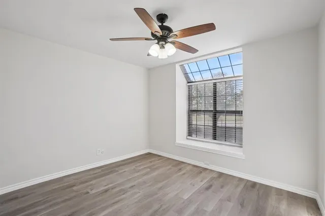 an empty room with wooden floor fan and windows