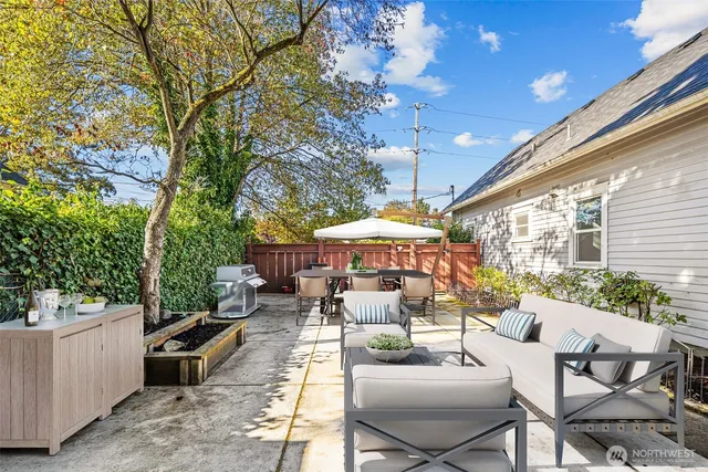 a view of a patio with couches table and chairs under an umbrella with a large tree