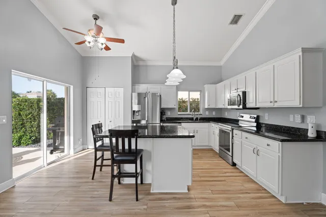a kitchen with stainless steel appliances granite countertop a dining table chairs stove and white cabinets