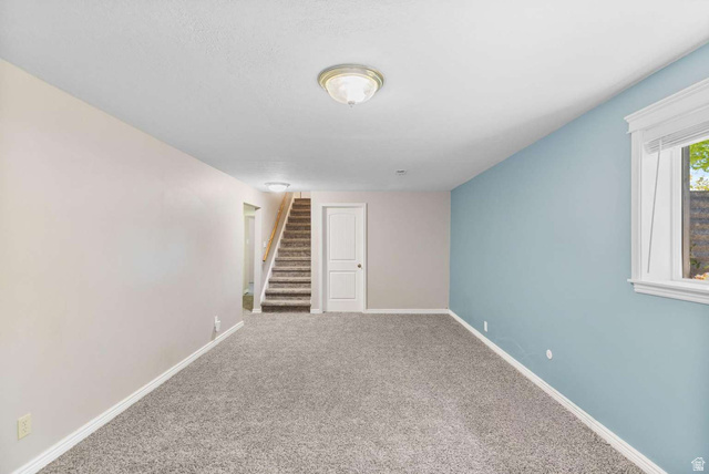 415 East 1150th Street North Logan, UT 84341 - Photo 21 of 38 Spacious room featuring carpeting, a light blue accent wall, a contrasting light gray wall, a window with blinds, and a staircase with wood-finish handrails