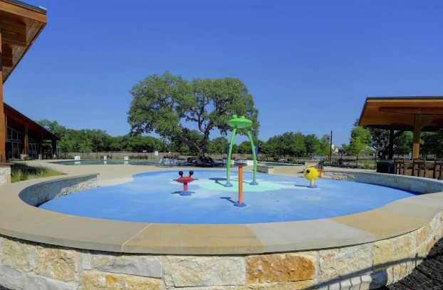 3625 Garrano Bend Leander, TX 78641 - Photo 36 of 38 Outdoor splash pad featuring a blue and light blue surface, multiple water features, and a stone-clad perimeter wall