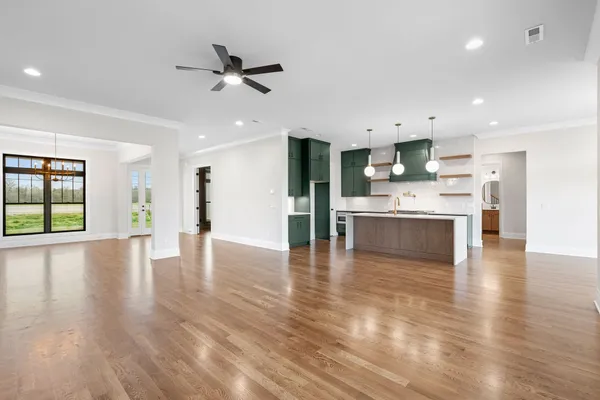 a view of an empty room and kitchen with window wooden floor and a ceiling fan