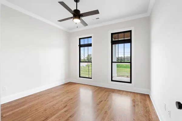an empty room with wooden floor fan and windows