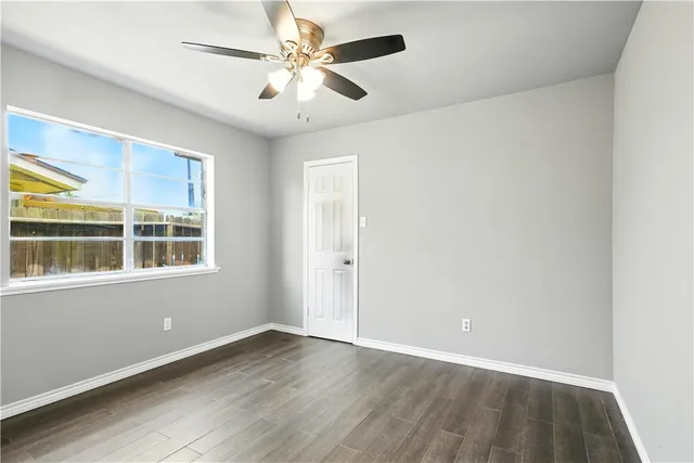 an empty room with wooden floor chandelier fan and windows
