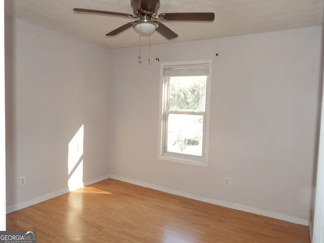 an empty room with wooden floor fan and windows