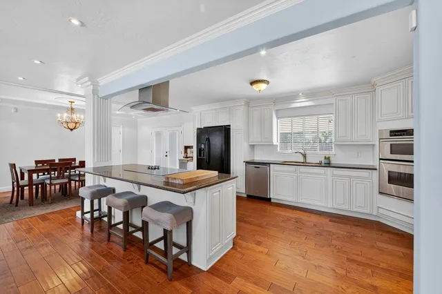 a kitchen with stainless steel appliances granite countertop a stove top oven a sink dishwasher a dining table and chairs with wooden floor