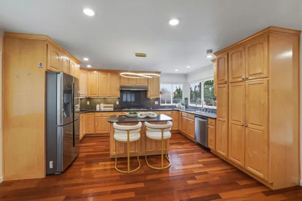 a kitchen with stainless steel appliances granite countertop a refrigerator a microwave oven a sink a dining table and chairs with wooden floor