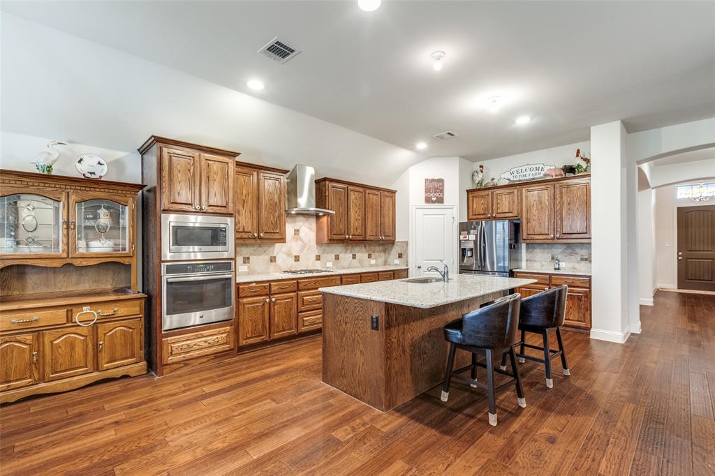 4217 Switchgrass Street Celina, TX 75009 - Photo 3 of 25 a kitchen with stainless steel appliances granite countertop a kitchen island hardwood floor sink stove dining table and chairs