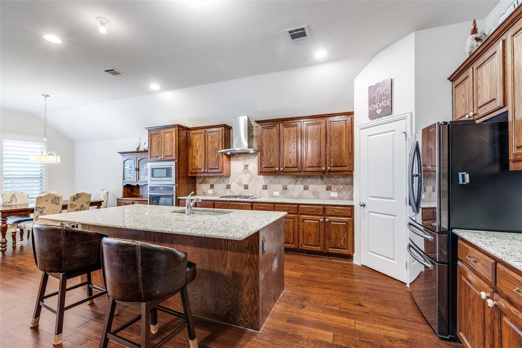 4217 Switchgrass Street Celina, TX 75009 - Photo 4 of 25 a kitchen with stainless steel appliances granite countertop a refrigerator a sink dishwasher a stove with chairs and wooden floor