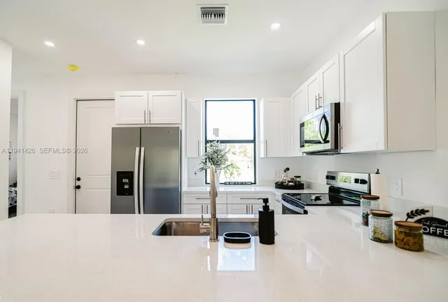 a kitchen with stainless steel appliances a refrigerator a sink a stove and white cabinets