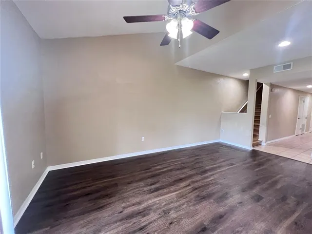 a view of an empty room with wooden floor and a ceiling fan