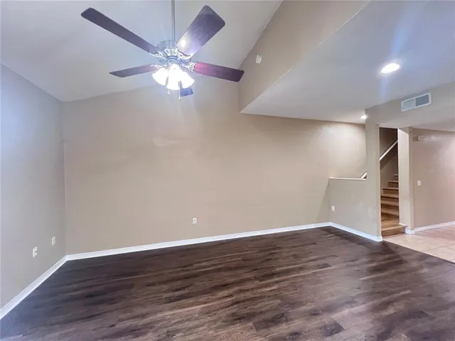 a view of an empty room with wooden floor and a ceiling fan