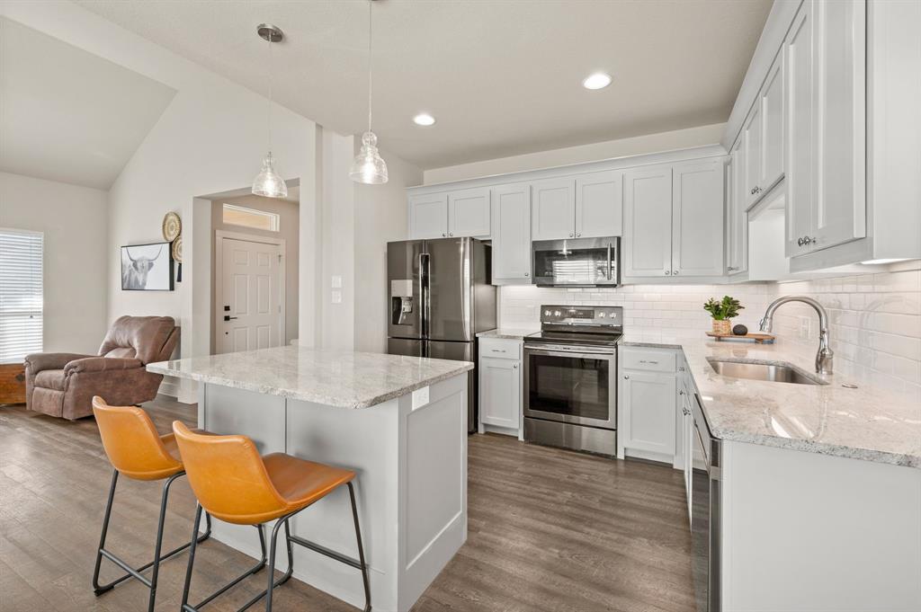 824 East Northside Drive Pilot Point, TX 76258 - Photo 7 of 23 a kitchen with stainless steel appliances a stove a sink a refrigerator white cabinets and wooden floor