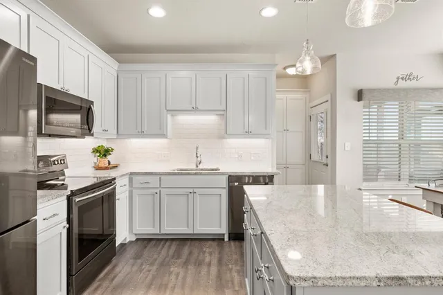 a kitchen with stainless steel appliances granite countertop a sink stove a refrigerator a microwave oven with white cabinets and wooden floor