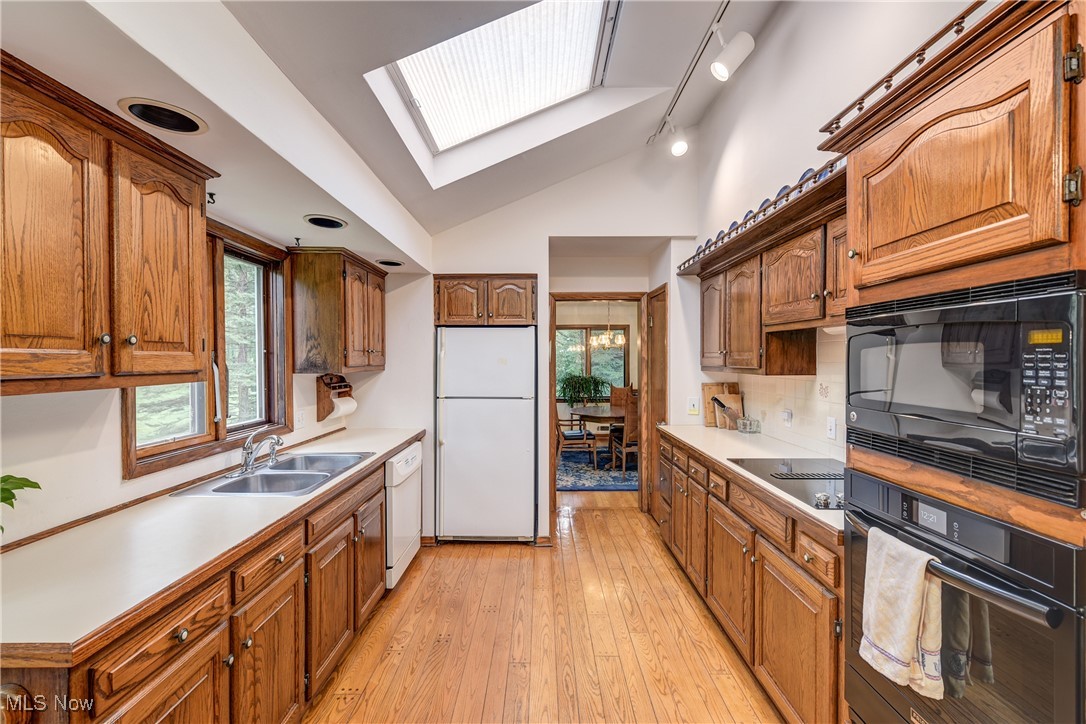 4712 Hillside Road Independence, OH 44131 - Photo 14 of 47 Kitchen featuring vaulted ceiling, brown cabinets, a skylight, black appliances, and light countertops