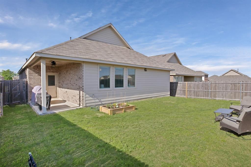 621 Ridgeback Trail Fort Worth, TX 76052 - Photo 17 of 22 Spacious backyard featuring a covered patio with a ceiling fan, a large expanse of green lawn, a wooden privacy fence, and a raised garden bed