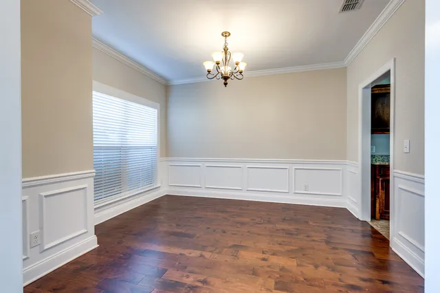 an empty room with wooden floor chandelier and windows