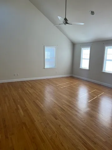 an empty room with wooden floor chandelier fan and windows