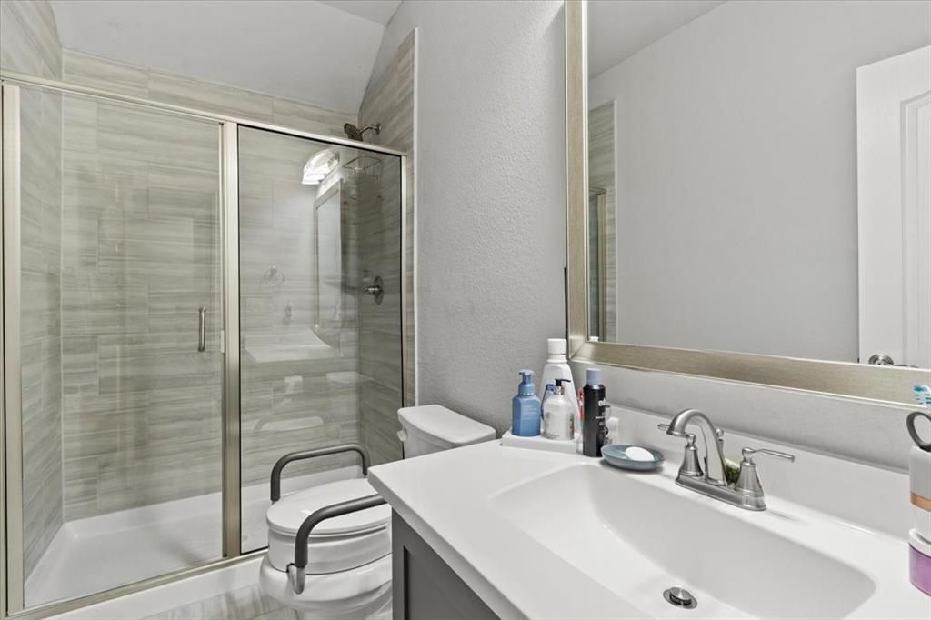 620 Shadow Trail Frisco, TX 75033 - Photo 33 of 36 Bathroom featuring a glass-enclosed shower with horizontal tile surround, a white vanity with integrated sink, chrome faucet, and a large framed mirror