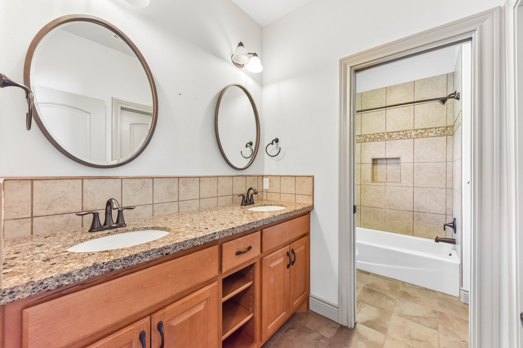 163 Powder Horn Road Bastrop, TX 78602 - Photo 19 of 34 Double vanities with stone countertops stand adjacent to a tiled tub and shower area.